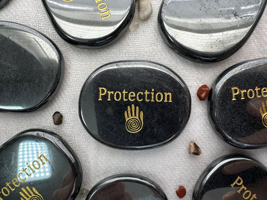 Flat hematite palm stone, with shaman hand printed along with the word protection in gold ink